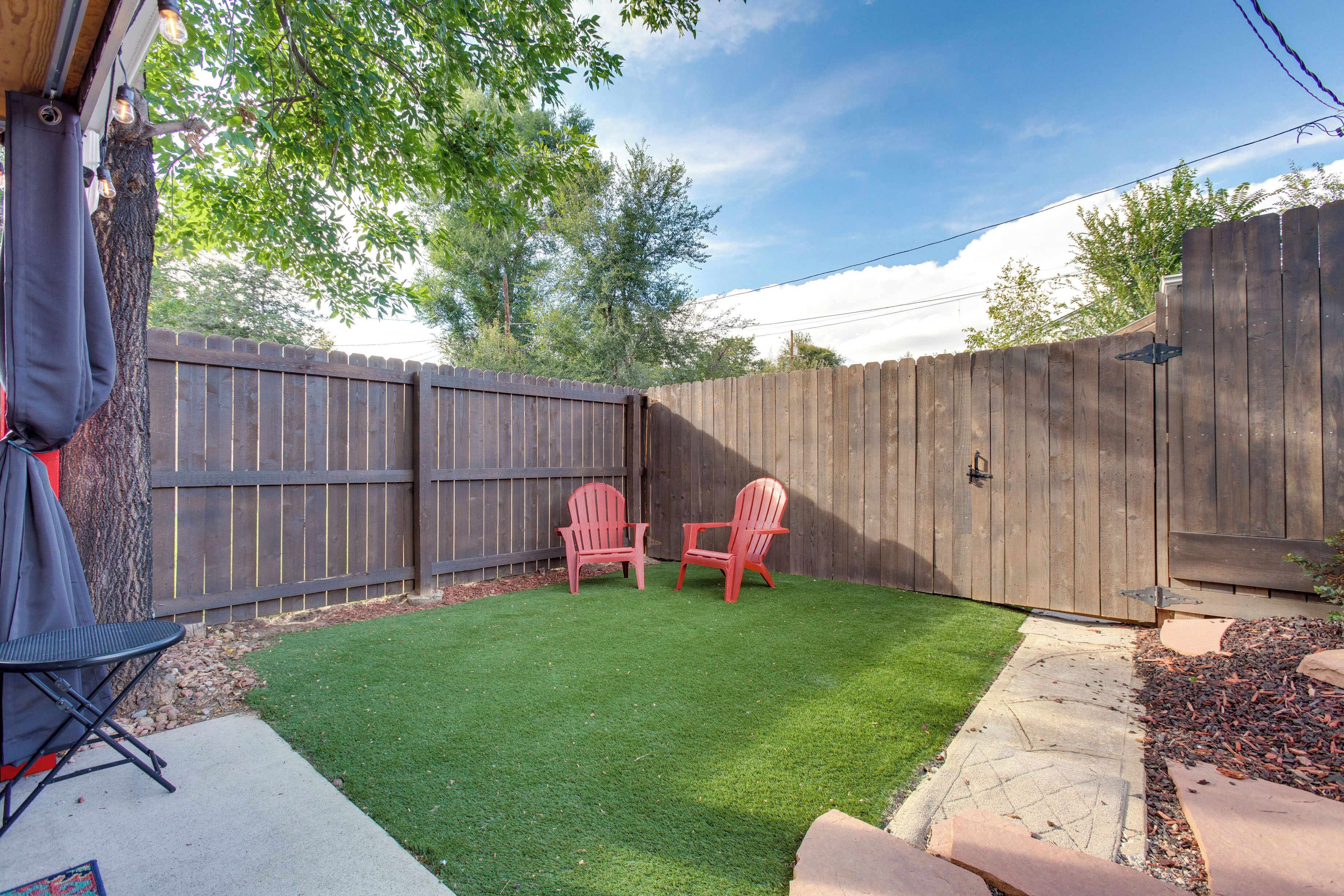 A backyard with artificial grass, two red chairs, a barbecue grill, and a wooden fence.