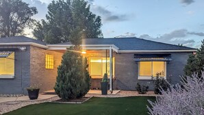 A two-story house with a covered porch, a small garden with a lawn and potted plants, and a well-maintained exterior. - Location! Outdoor Living Hot Tub Walkable Denver (Edgewater)
