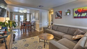 A living room with a sofa, coffee table, and decorative pillows. There is a dining area with a table and chairs. The room has a neutral color scheme and features artwork on the walls. - Location! Outdoor Living Hot Tub Walkable Denver (Edgewater)