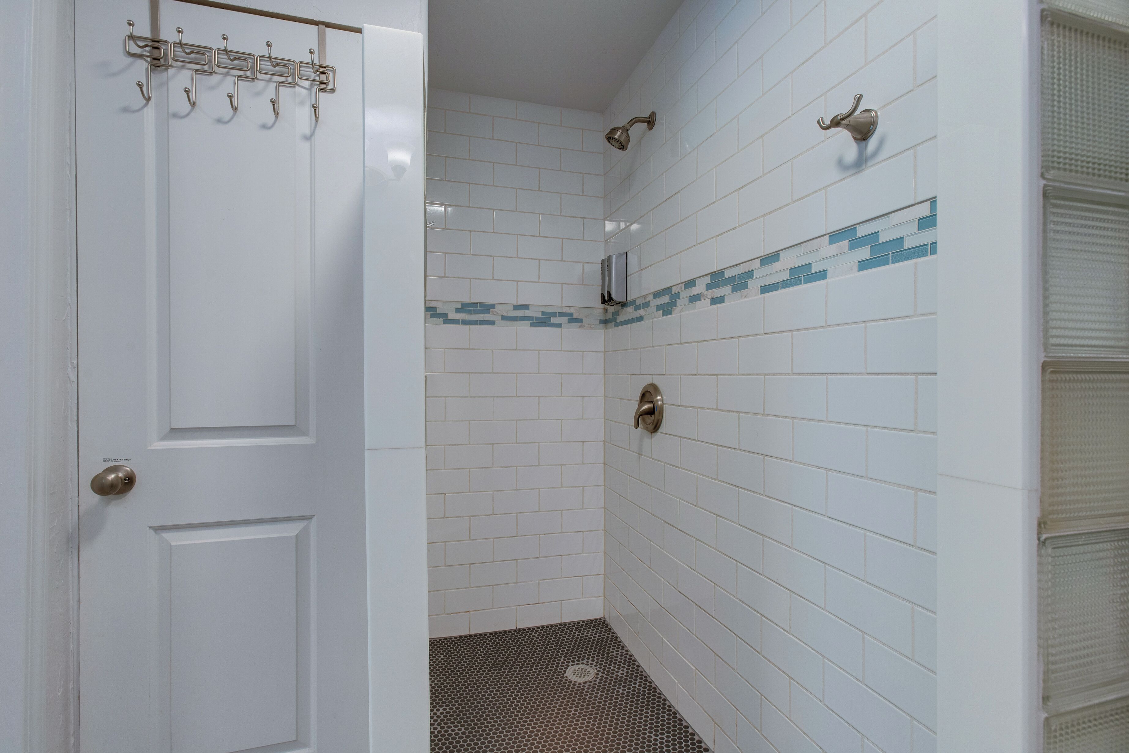 A bathroom with white tiled walls, a shower area, and a door with a coat hook.