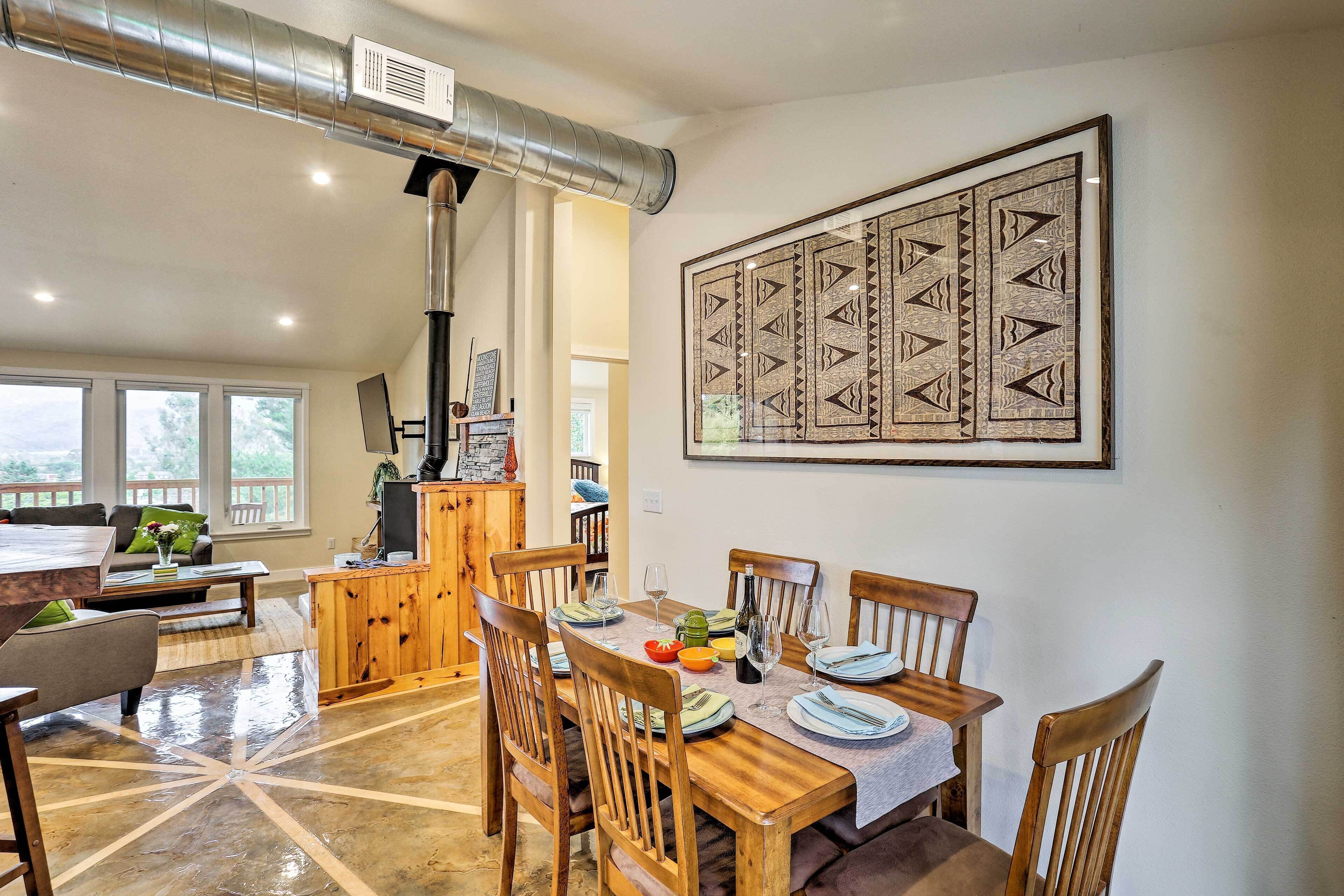 Un comedor con una mesa de madera dispuesta para cuatro personas, rodeada de sillas de madera. Encima de la mesa, una pieza decorativa de gran tamaño.