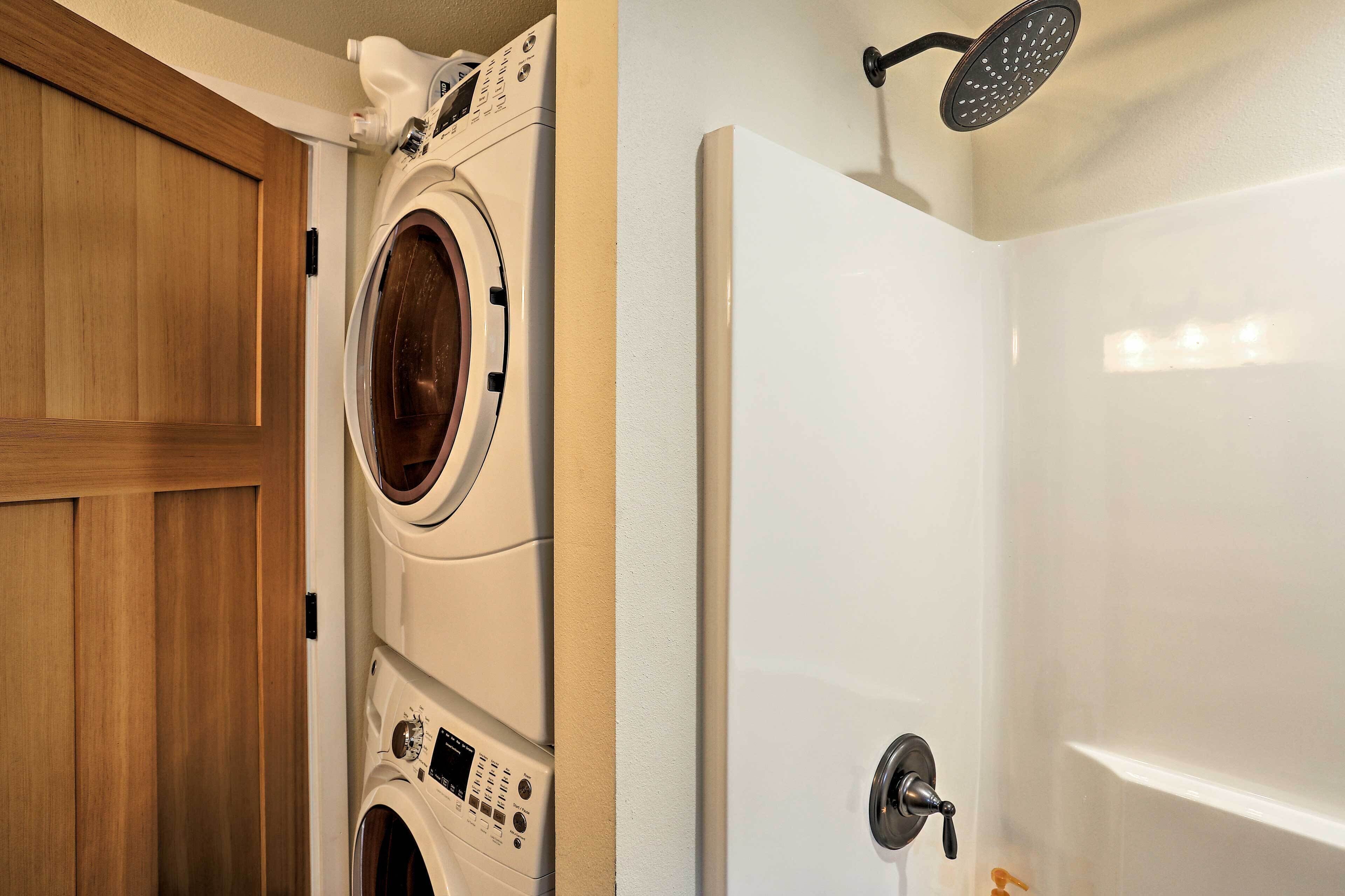 A laundry area with a front-loading washer and dryer, a wooden door, and a shower with a handheld showerhead.