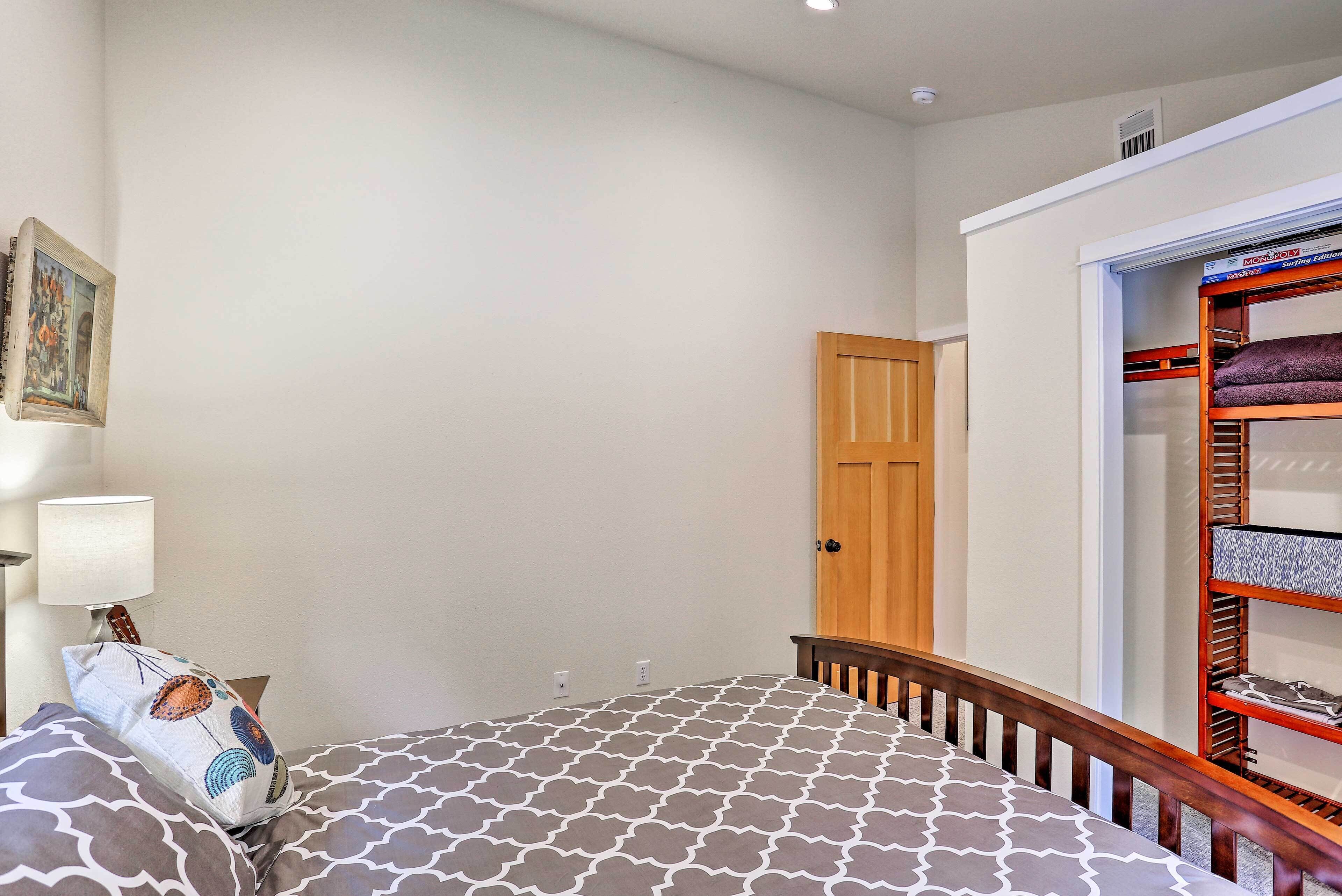 A bedroom with a patterned bedspread, a wooden headboard, a nightstand with a lamp, a wall-mounted picture, and a closet with shelves.