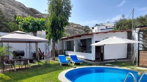 Um quintal com piscina, duas espreguiçadeiras, área de churrasco e varanda coberta.
