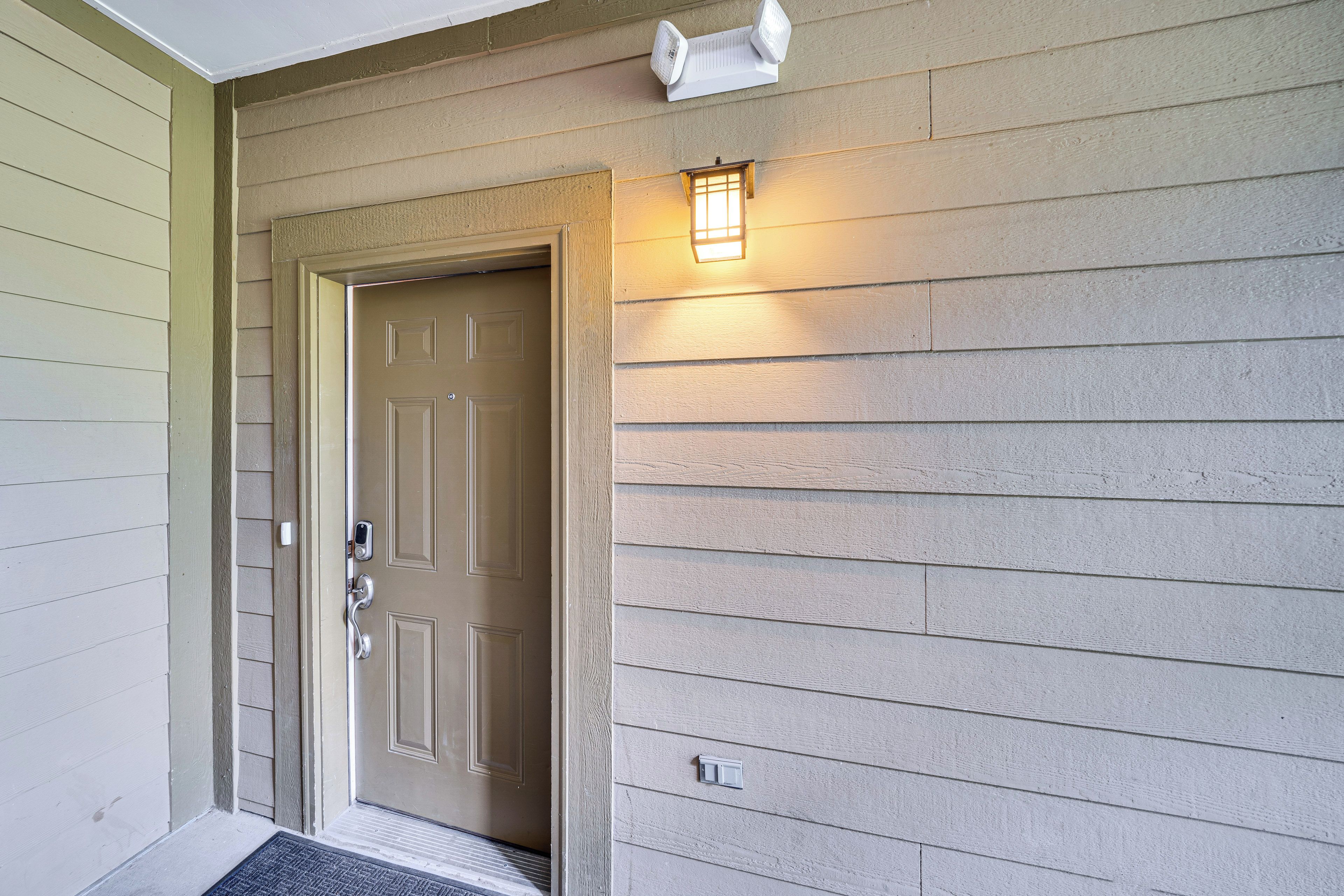 A house entrance with a beige door, a small porch, and a wall-mounted light fixture.