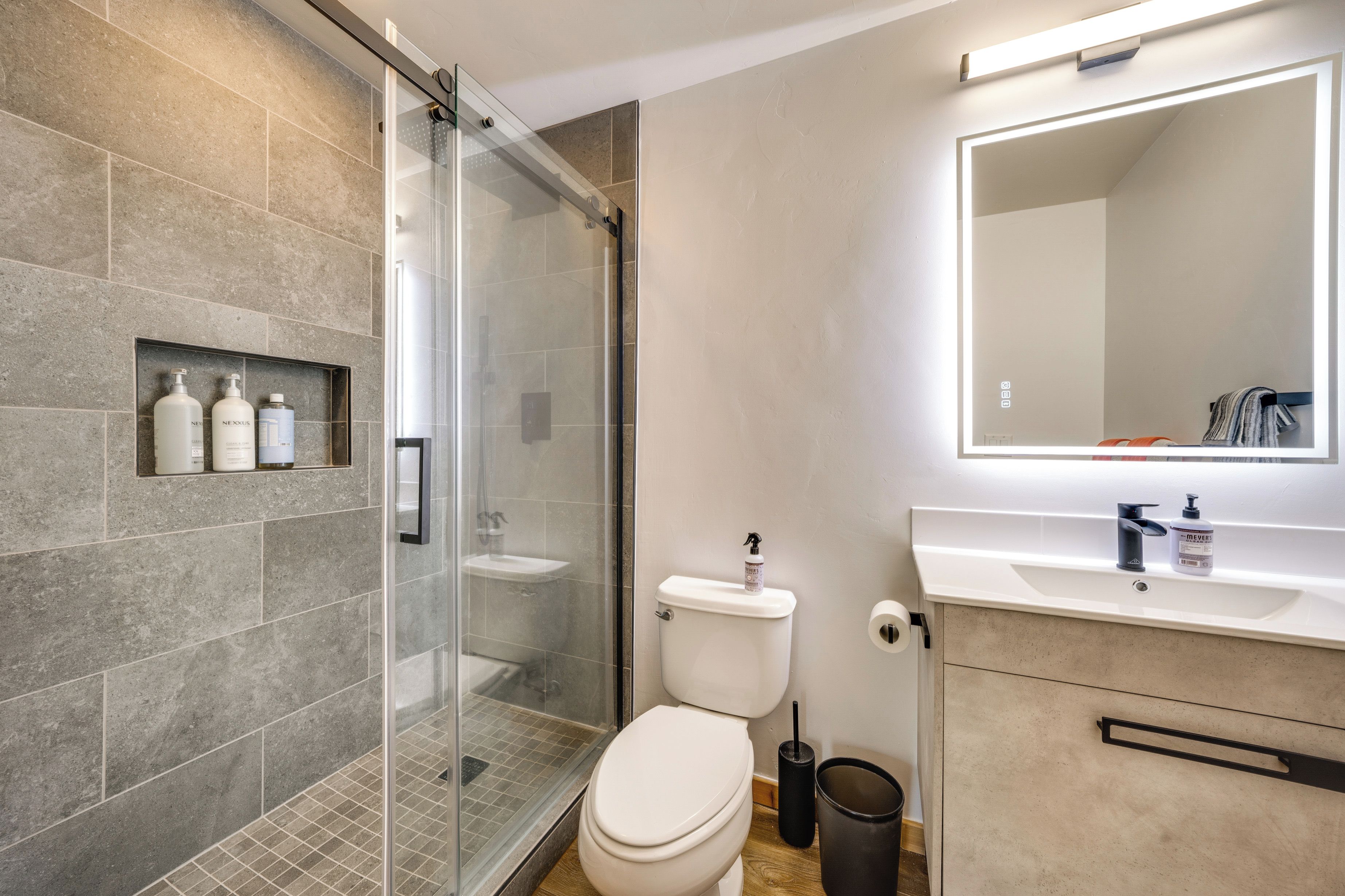 A modern bathroom with a glass shower enclosure, a toilet, and a vanity with a mirror.