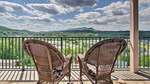 Un balcon doté de fauteuils en osier, offrant une vue panoramique sur un paysage magnifique, avec des montagnes et une végétation luxuriante.