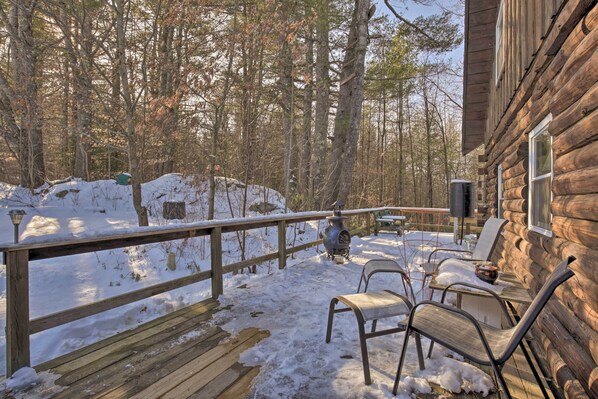 A wooden cabin with a deck, outdoor seating, and a snow-covered ground.