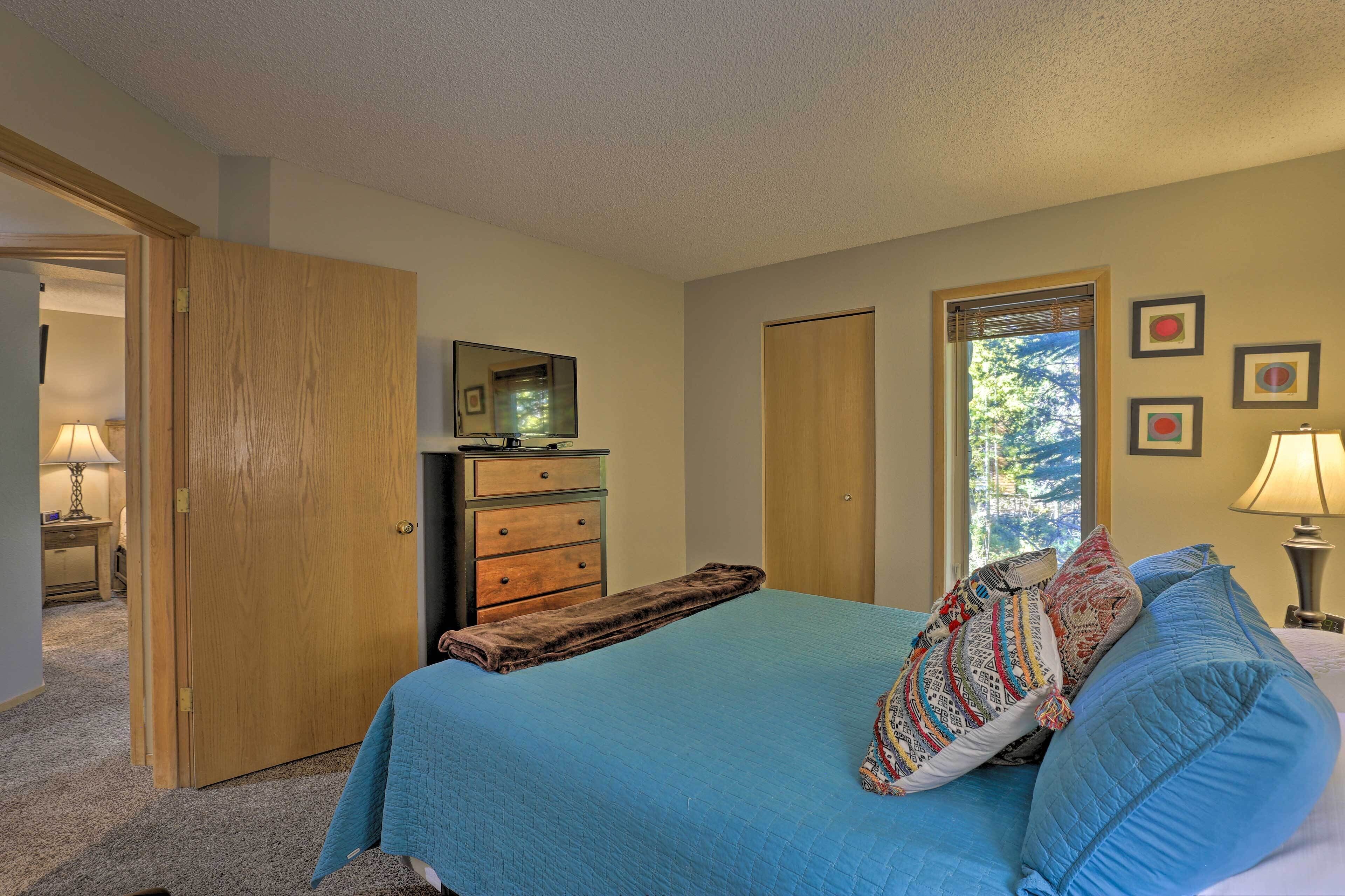 A bedroom with a bed, a dresser, a television, and a window with blinds.