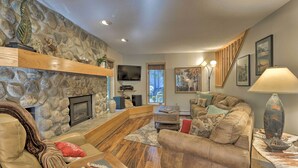 A cozy living room with a stone fireplace, comfortable seating, and a television. - Creekside Frisco Condo w/ Views & Pool Access! (Frisco)
