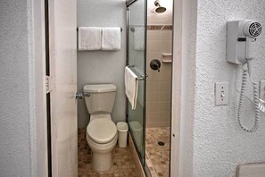 A bathroom with a toilet, a glass shower enclosure, and a hairdryer mounted on the wall. - Bolongo Bay Oceanfront Condo w/ Community Pool! (St. Thomas)