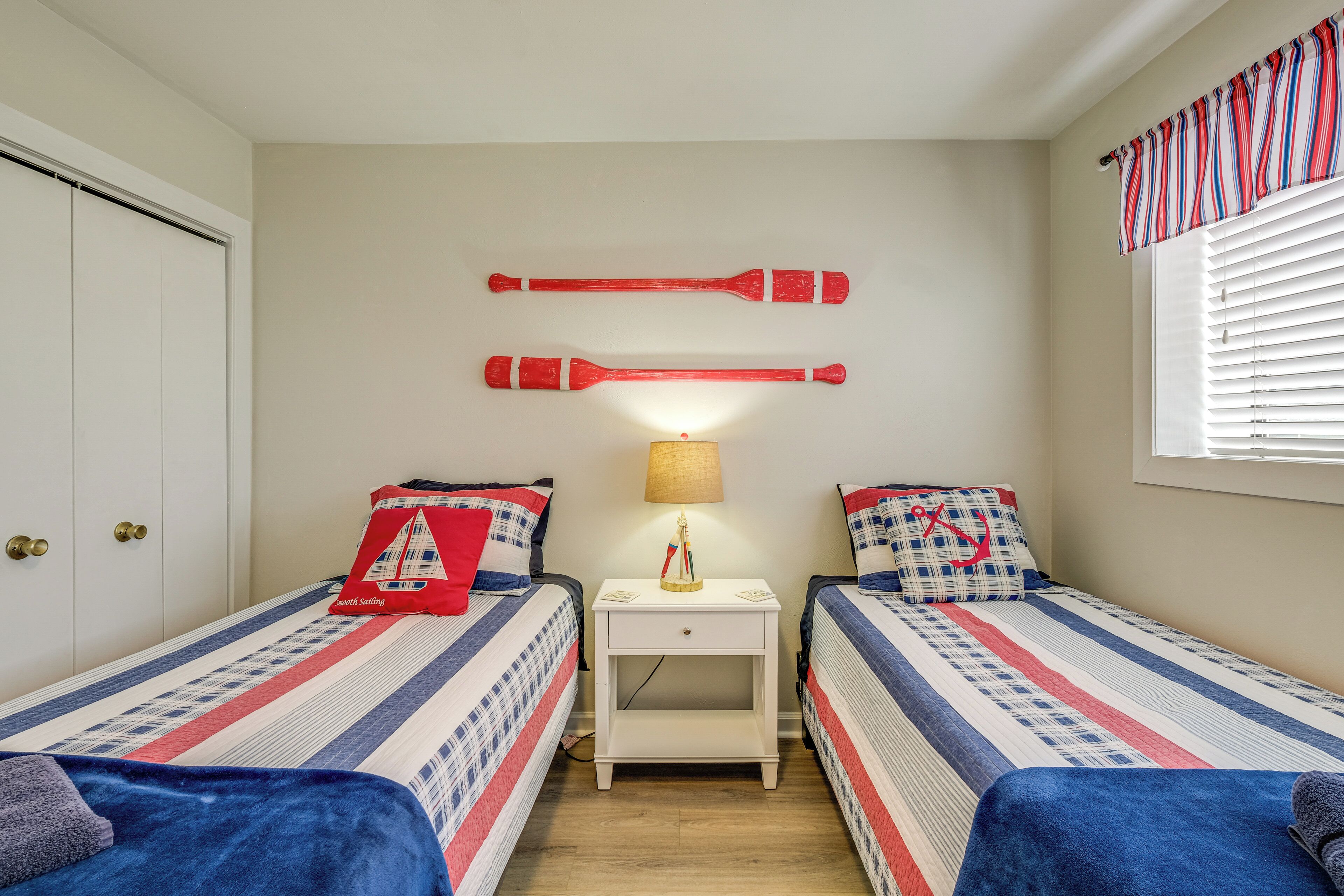 Une chambre avec deux lits, une table de chevet, une lampe et une fenêtre avec des stores.