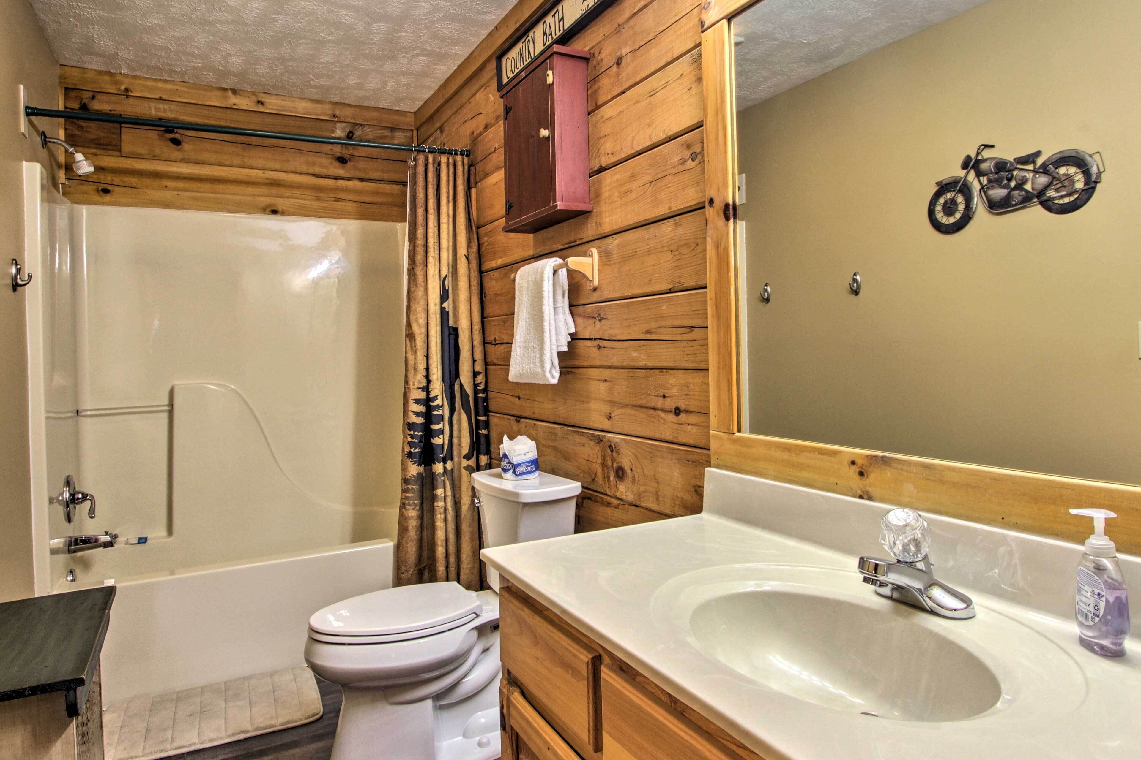 A bathroom with a bathtub, toilet, wooden wall paneling, a mirror, and a motorcycle decal.