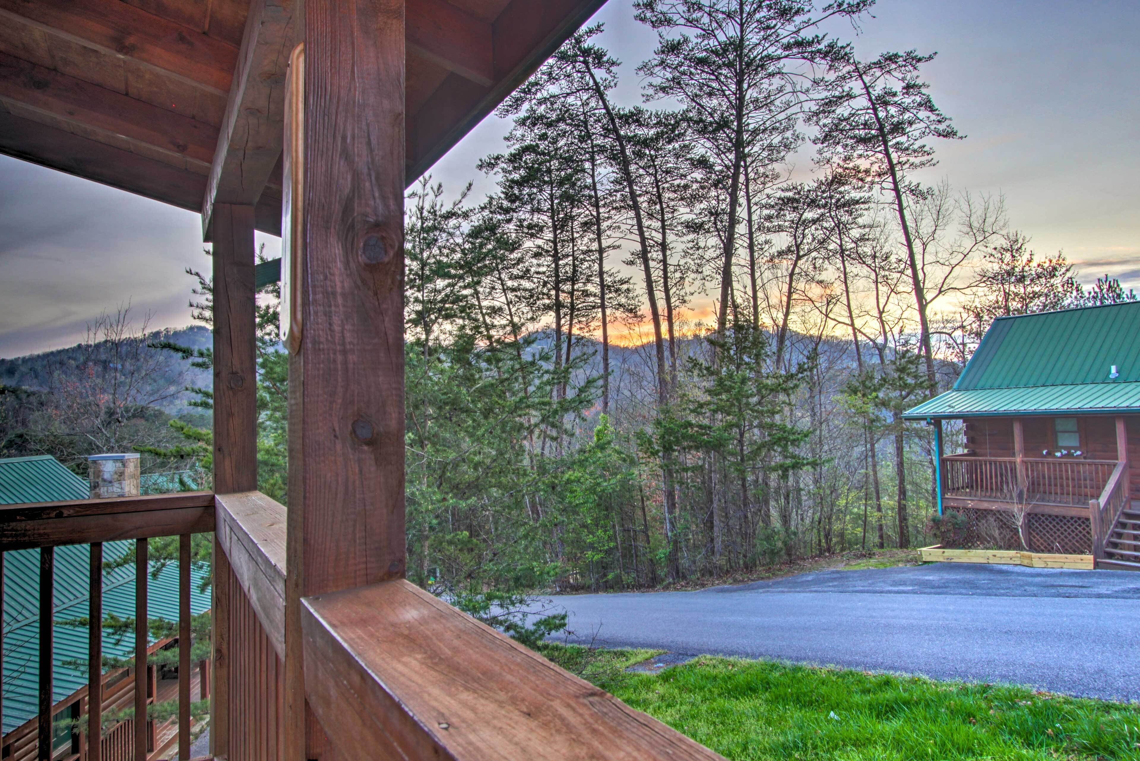 A wooden cabin with a porch overlooking a forested area and a mountain range.