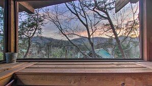Eine hölzerne Bank mit Blick auf einen Wald und Berge durch ein Fenster.