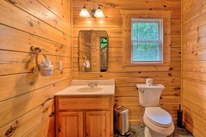 A wooden cabin bathroom with a sink, toilet, and a window with blinds.