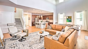 A spacious living area with a leather sofa, a white armchair, and a patterned rug. A dining table with chairs is visible in the background.