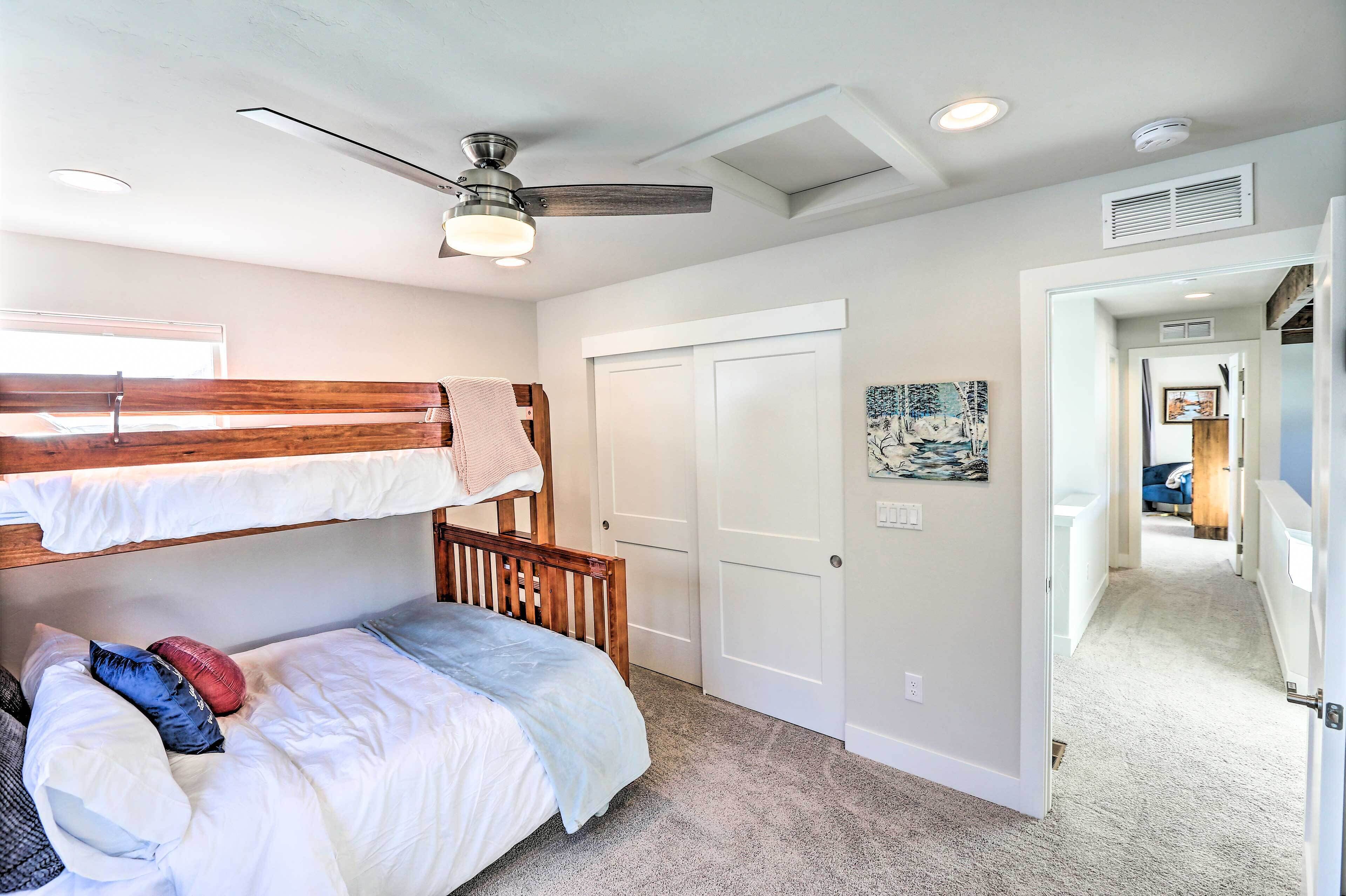 A bedroom with bunk beds, a ceiling fan, and a door leading to another room.