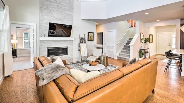 A spacious living room with a brown leather sofa, a fireplace, a flat-screen TV, and a staircase leading to an upper level.