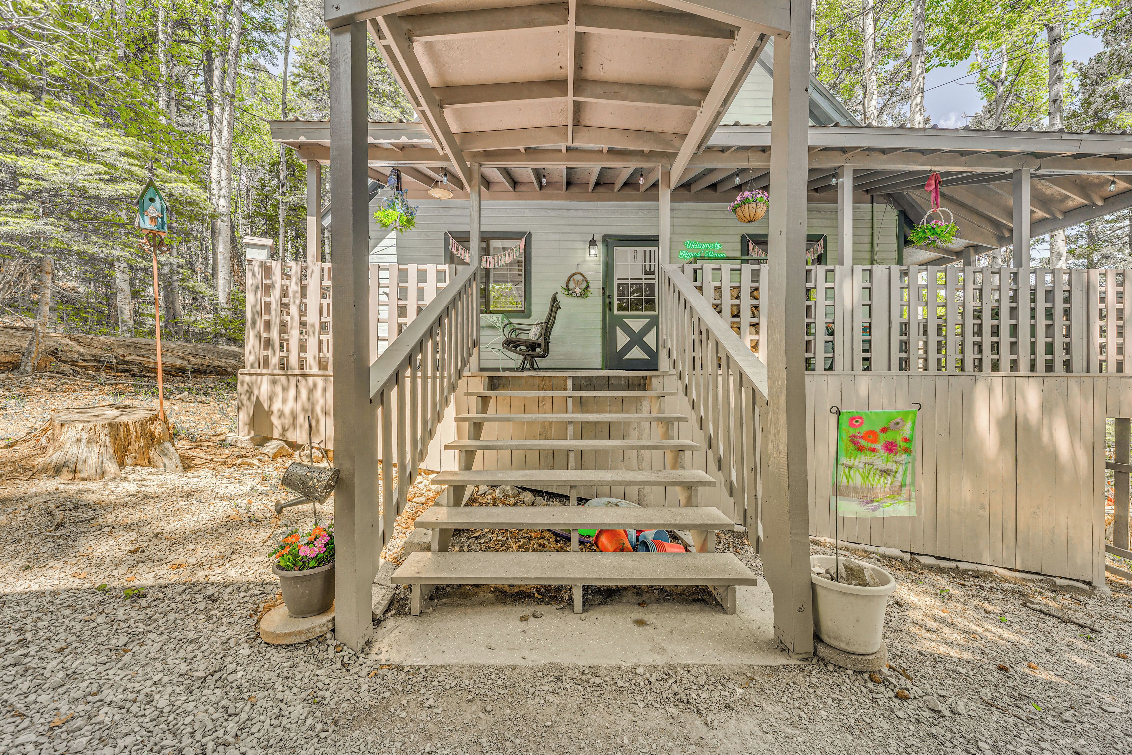 A wooden staircase leading to a covered porch with a bench, surrounded by a wooden fence and trees.