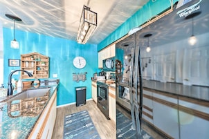 A modern kitchen with blue walls, a wooden shelf, a clock, and stainless steel appliances.