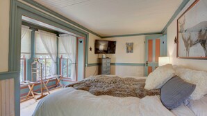 Un dormitorio con cama, cómoda, televisor y ventana con cortinas.