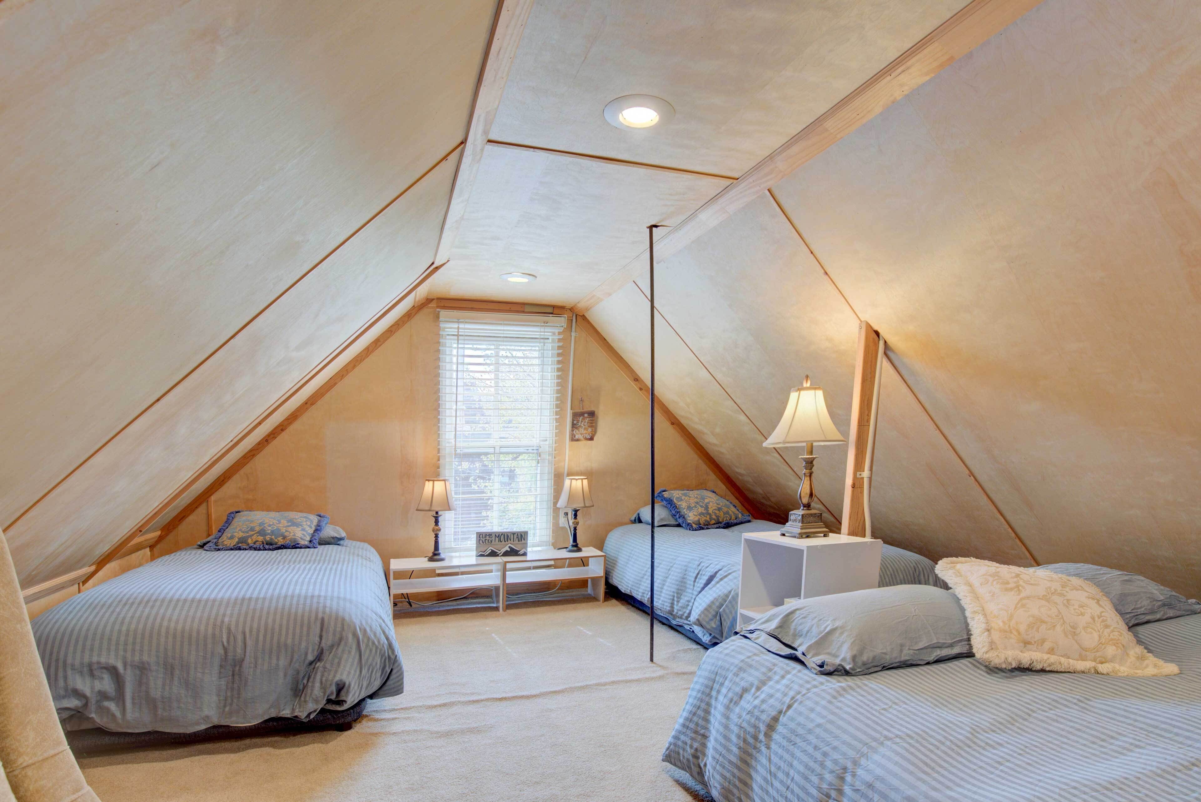 Une chambre mansardée chaleureuse, dotée de deux lits, d’une fenêtre avec stores et d’une petite table de chevet avec une lampe.