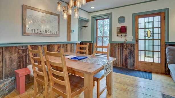 Una mesa de comedor de madera con sillas, un mapa enmarcado en la pared y una puerta de madera con un ventanal.