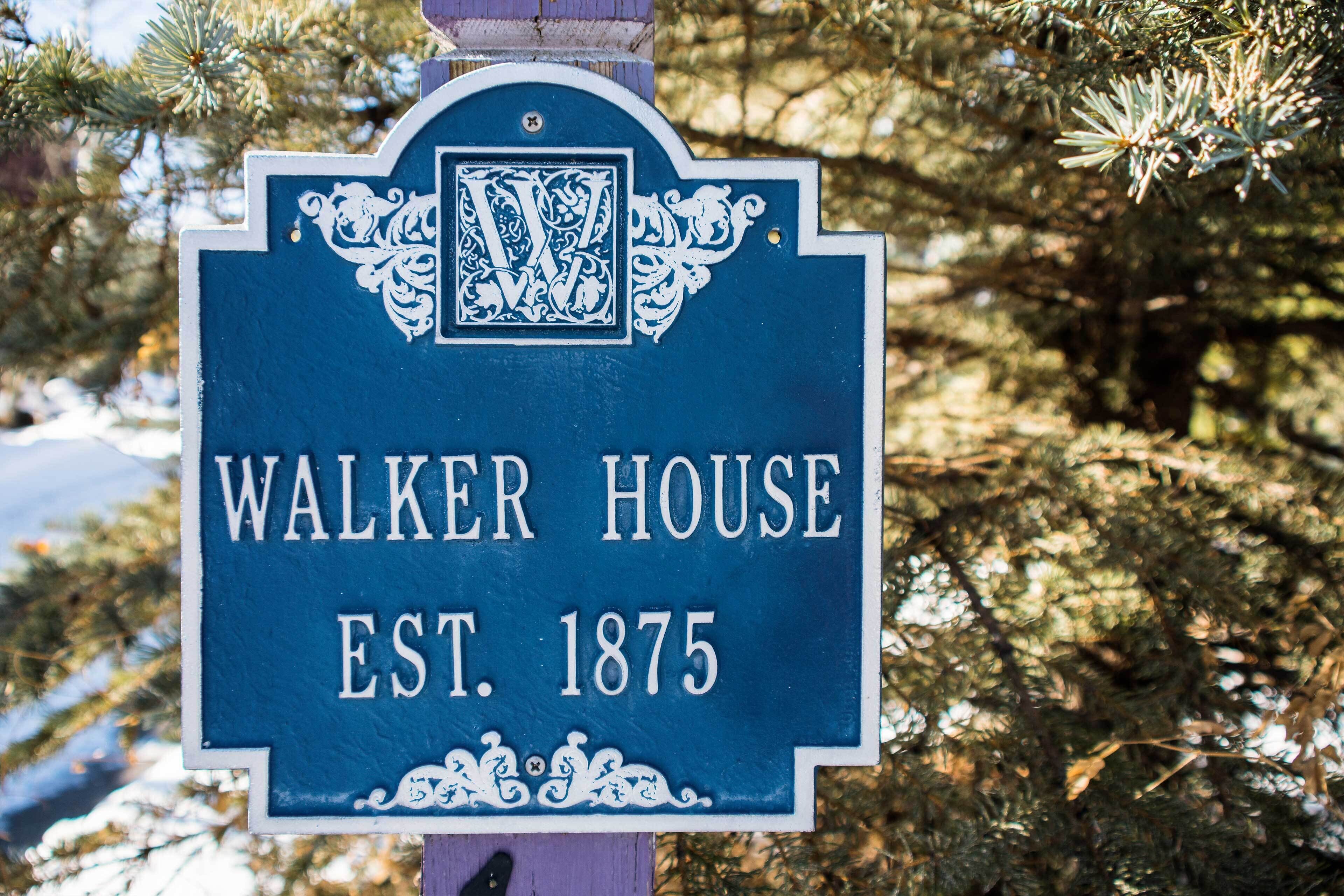 Un panneau bleu indiquant un site historique, celui de la maison Walker, construite en 1875, et entouré d’arbres.