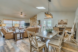 A spacious living area with a wooden dining table, leather sofas, and a stone accent wall. - 'winnie's Cabin' Ruidoso Retreat: Deck + Mtn Views (Ruidoso)