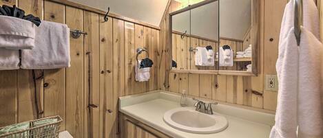 A wooden-paneled bathroom with a white sink, a mirror, and multiple towels hanging on hooks.