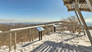 A wooden observation deck with metal railings and informational signs, overlooking a snowy landscape with distant hills. - Bright Wintergreen Resort Home; Deck & Grill! (Roseland)