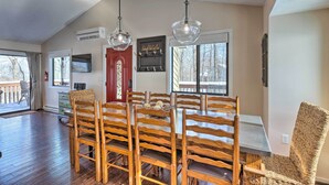 A dining area with a wooden table and chairs, a red door, and a window with a view of trees. - Bright Wintergreen Resort Home; Deck & Grill! (Roseland)