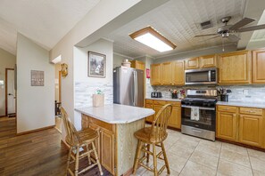 A kitchen with wooden cabinets, a stainless steel refrigerator, a microwave, and an oven. There is a wooden island with two chairs. - Expansive Angel Fire Home w/ Indoor Hot Tub! (Angel Fire)