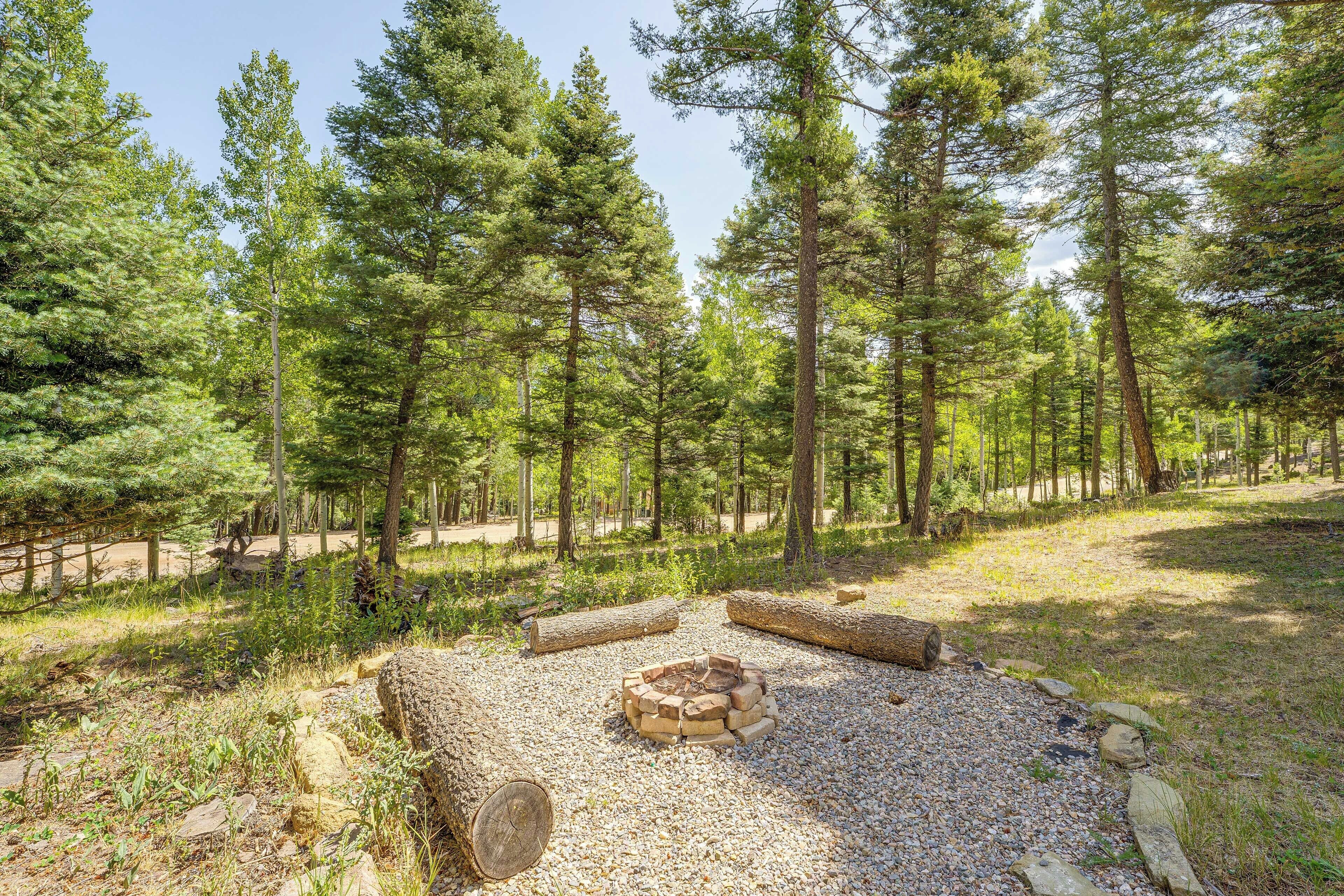 Ein von Bäumen umgebener Campingplatz mit Feuerstelle, umgeben von Steinen und Baumstämmen.