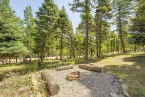 A forested campsite with a fire pit surrounded by rocks and logs. - Expansive Angel Fire Home w/ Indoor Hot Tub! (Angel Fire)