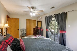 A bedroom with a bed, a wooden wardrobe, a chair, a desk, a ceiling fan, and a window with curtains.