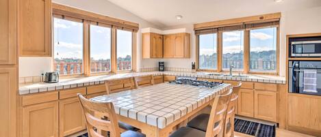 A modern kitchen with wooden cabinets, a tiled island, and large windows offering city views.