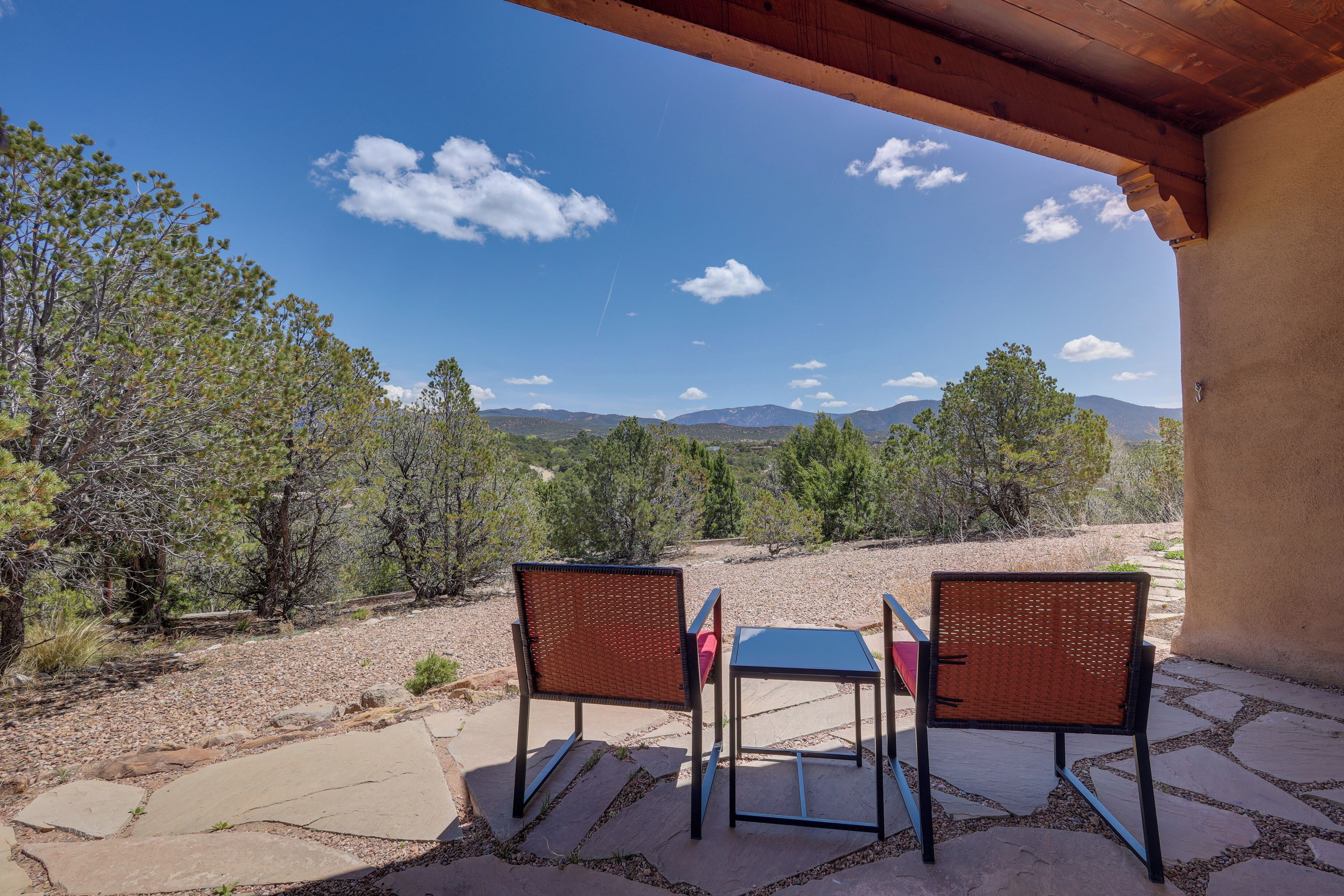 An outdoor patio with two wicker chairs and a small table, overlooking a mountainous landscape.
