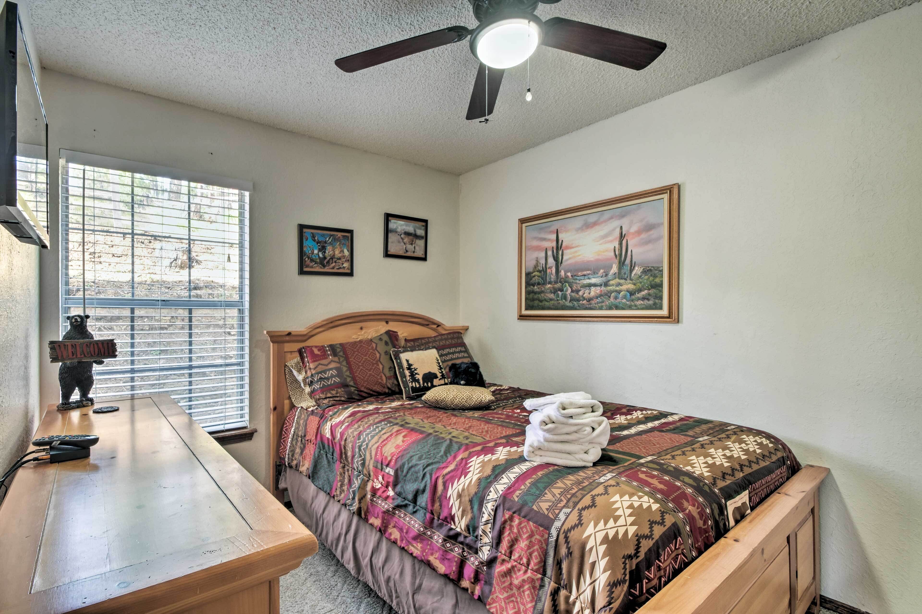 A bedroom with a bed, a desk, a ceiling fan, and a window with blinds.