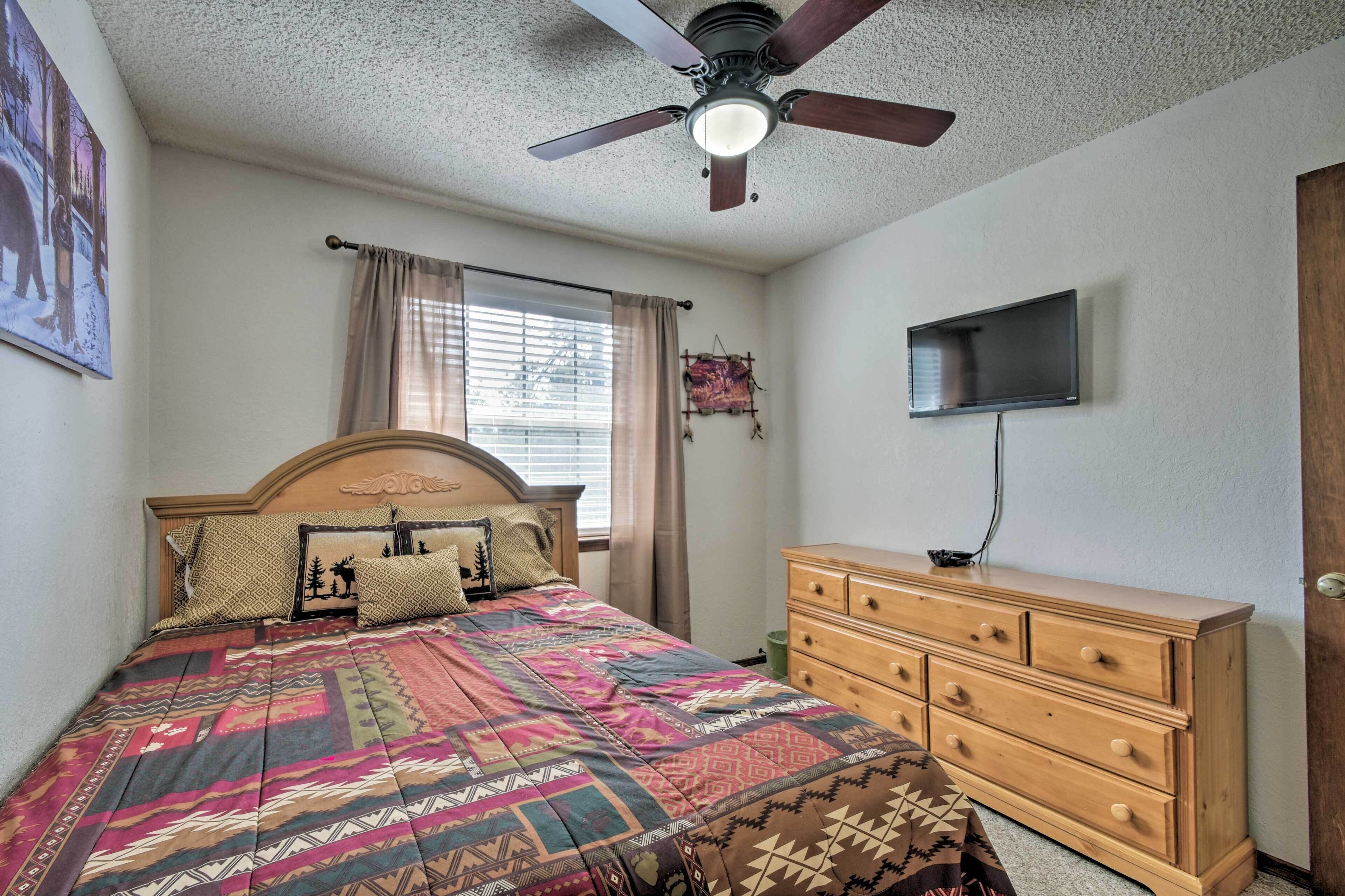 A bedroom with a bed, a ceiling fan, a dresser, a TV, and a window with curtains.