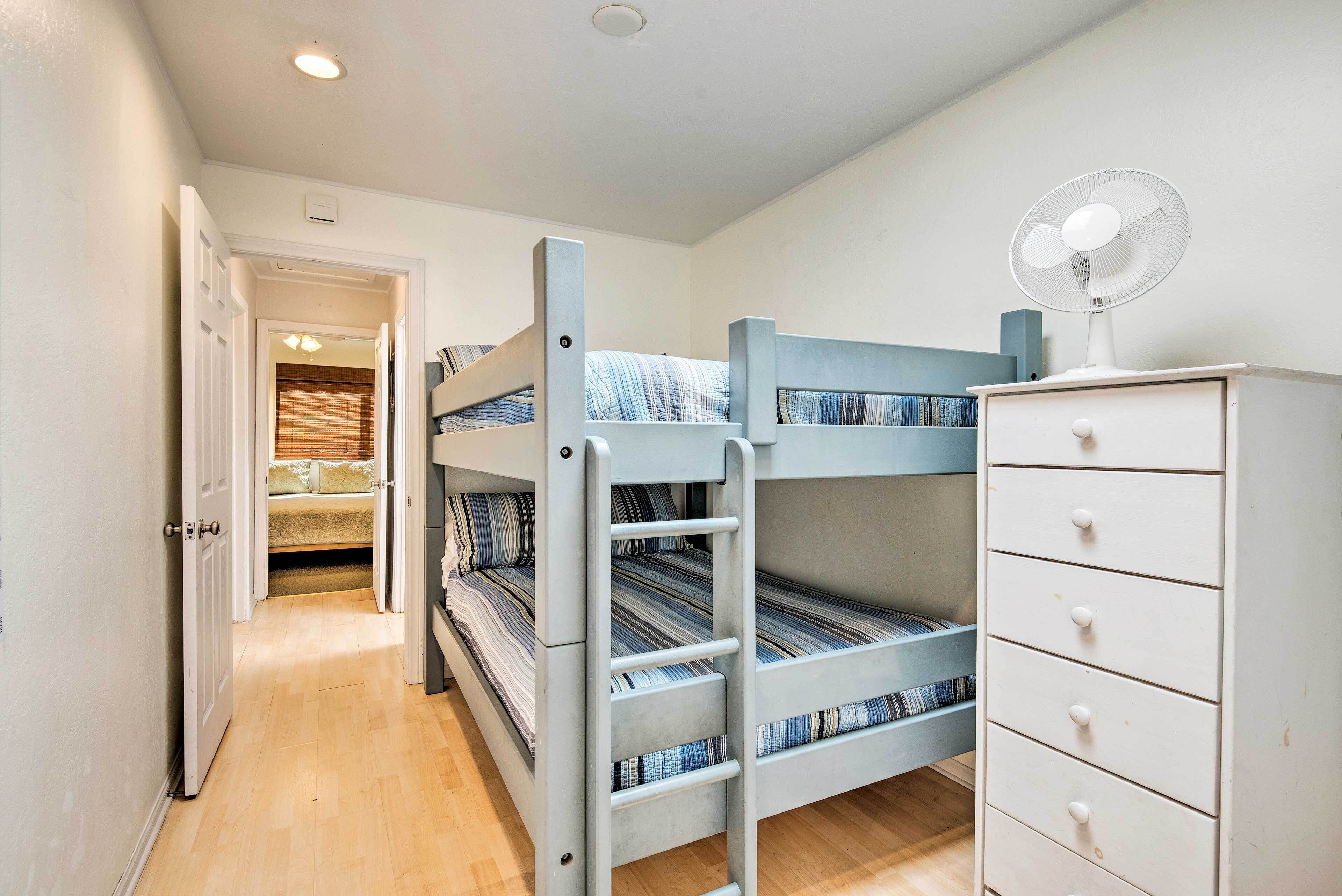 A bunk bed room with a ladder, a dresser, and a fan.