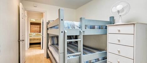 A bunk bed room with a ladder, a dresser, and a fan.