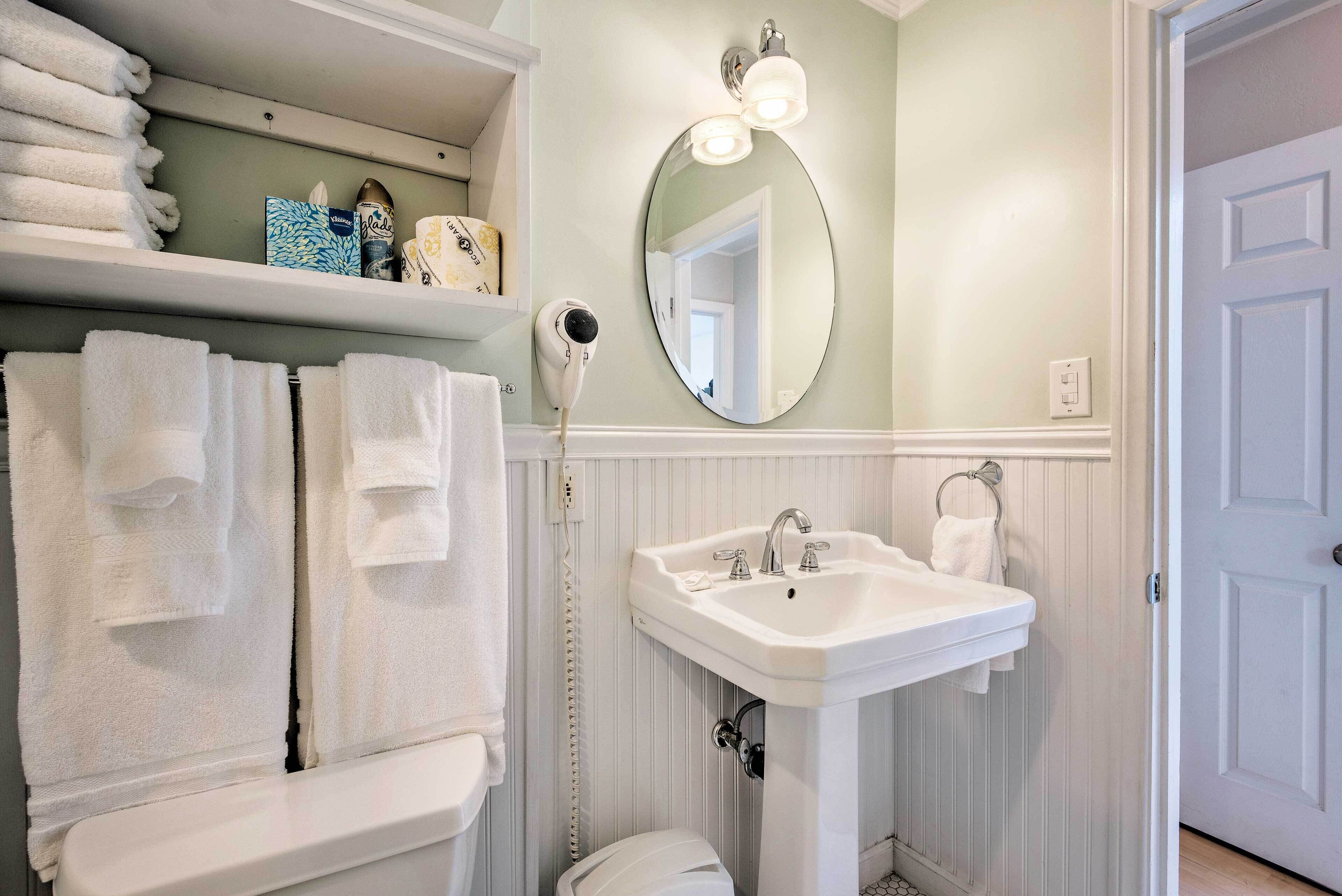 A bathroom with white towels, a sink, a mirror, and a hairdryer.