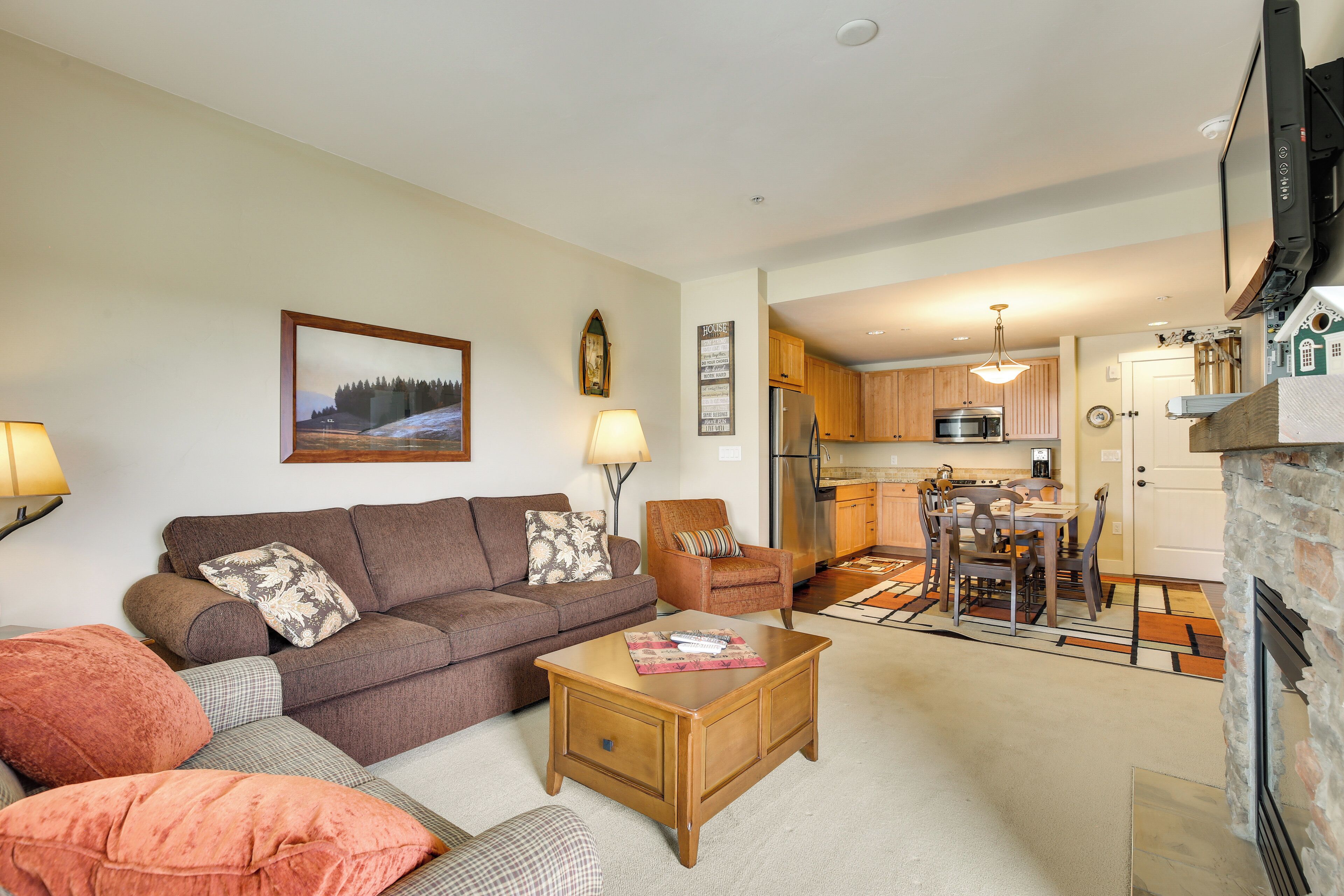 A living room with a sofa, armchair, and coffee table, a dining area with a table and chairs, and a kitchen with cabinets and appliances.