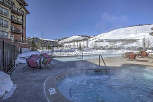 A hot tub area with chairs and a pool, surrounded by buildings and a snowy landscape.