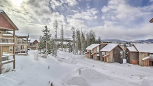 A snow-covered resort with multiple buildings, including cabins and a main lodge, surrounded by tall pine trees and mountains in the background. - Winter Park Area Retreat, Walk to Ski Shuttle (Fraser)