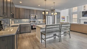 A modern kitchen with dark wood cabinets, stainless steel appliances, and a central island with a bench. - Winter Park Area Retreat, Walk to Ski Shuttle (Fraser)