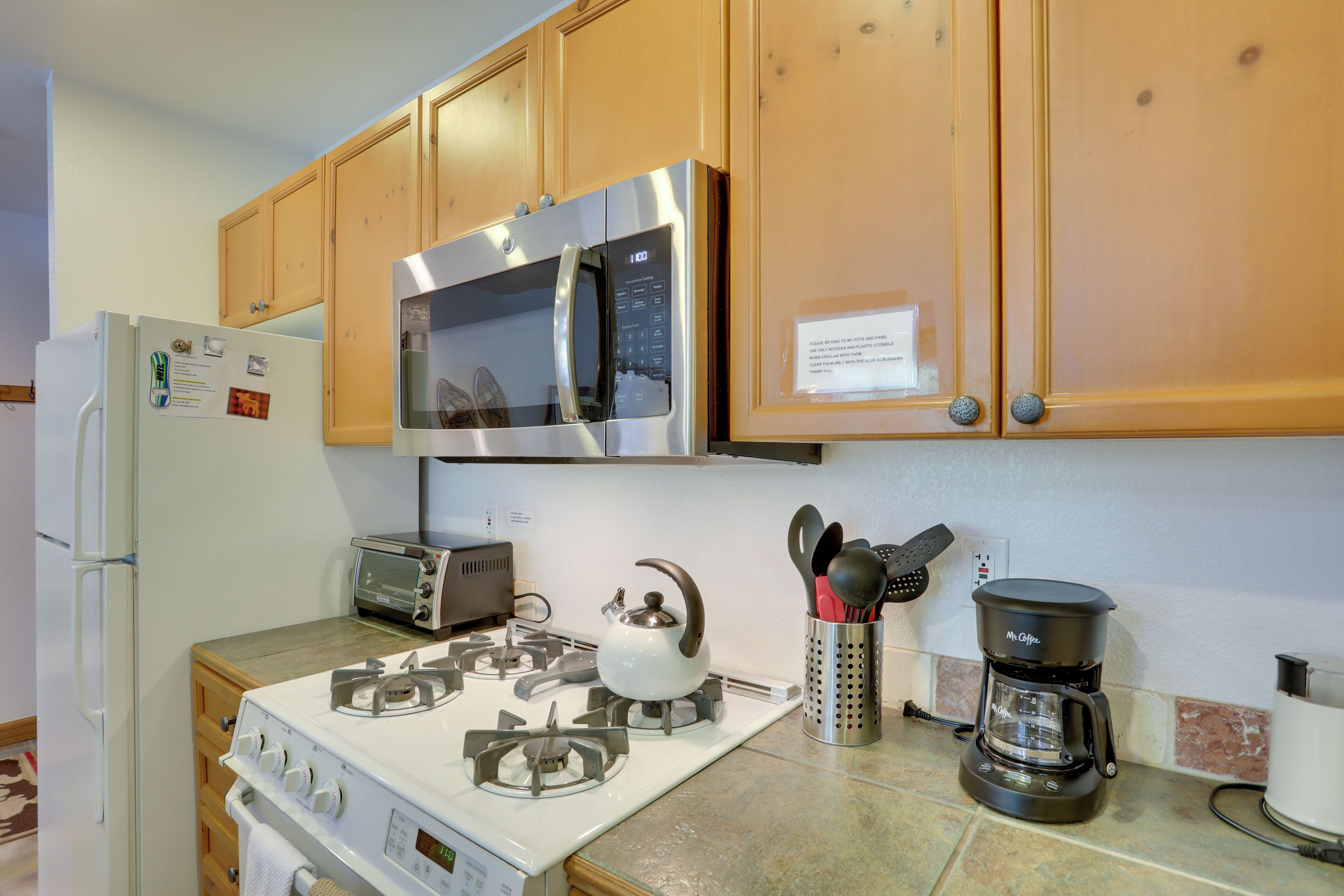 A kitchen with wooden cabinets, a stainless steel microwave, a gas stove, a toaster, and a coffee maker.