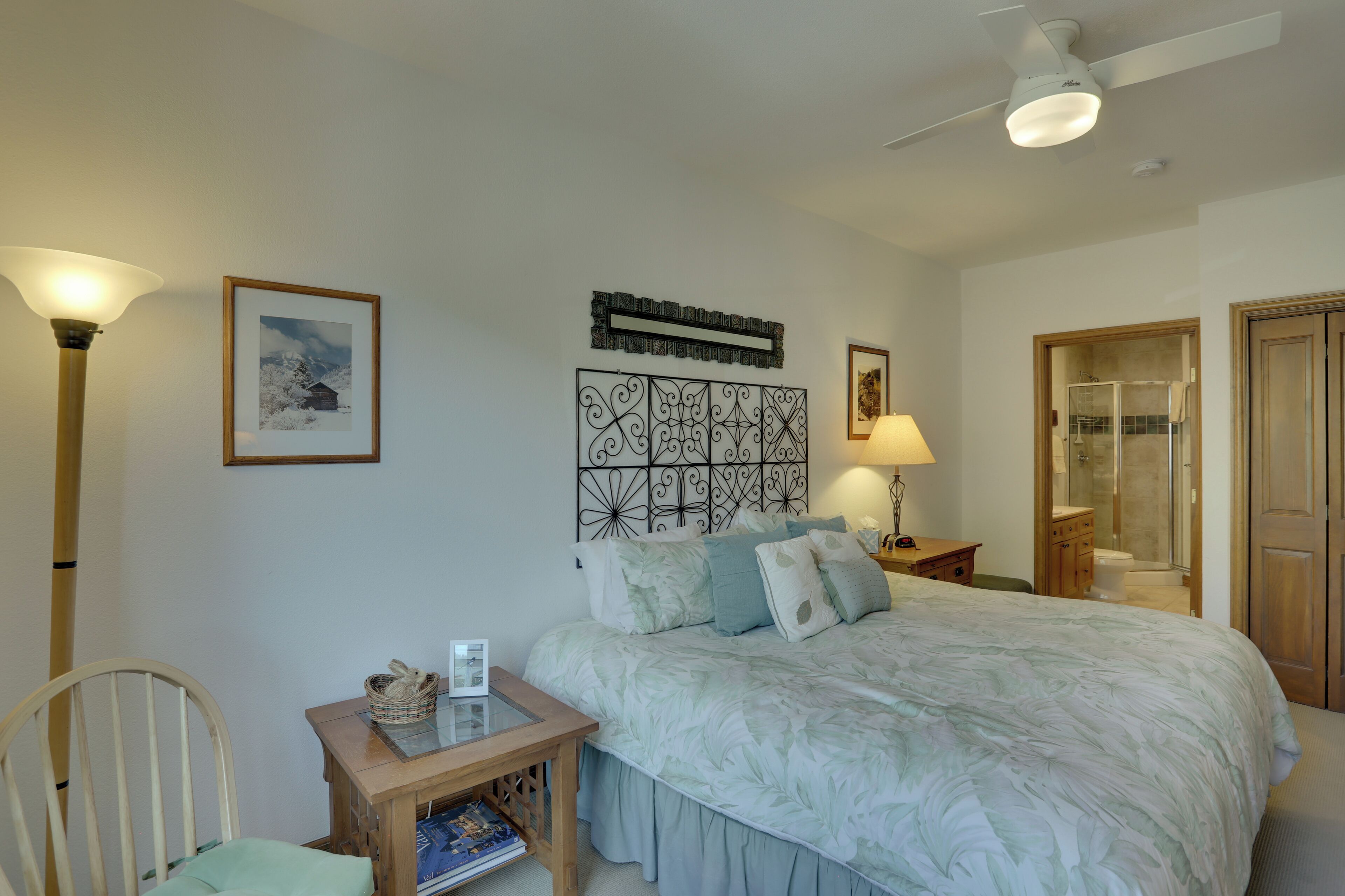 Quarto com uma cama grande, mesa de cabeceira com abajur, uma cadeira e um quadro na parede.